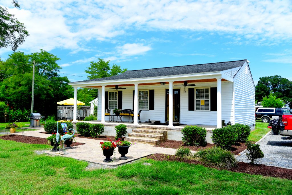 A white house has a porch with ceiling fans and furniture on it