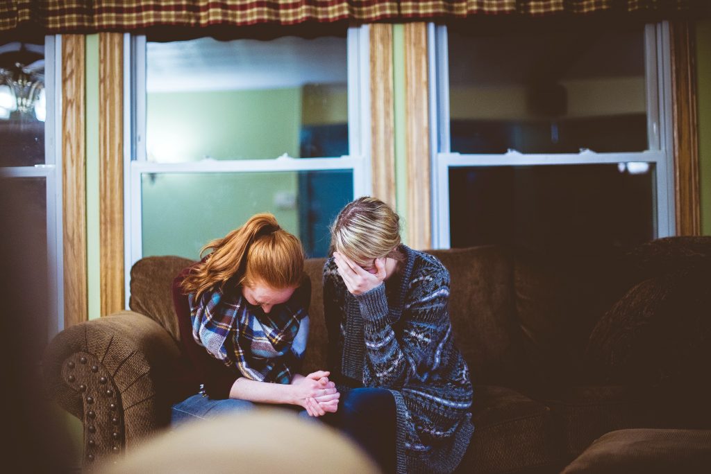 Two women sit on the couch with their heads in their hands.